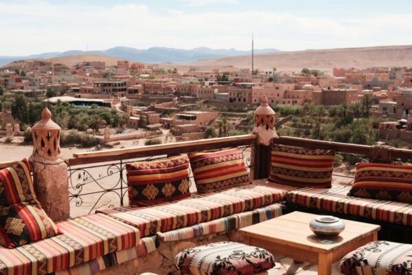 Dachterrasse mit bunten Sitzkissen und Blick über eine Oasenstadt in den Bergen von Marokko